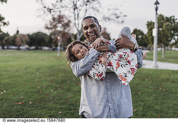 Happy father holding cute girl at park playground at dusk