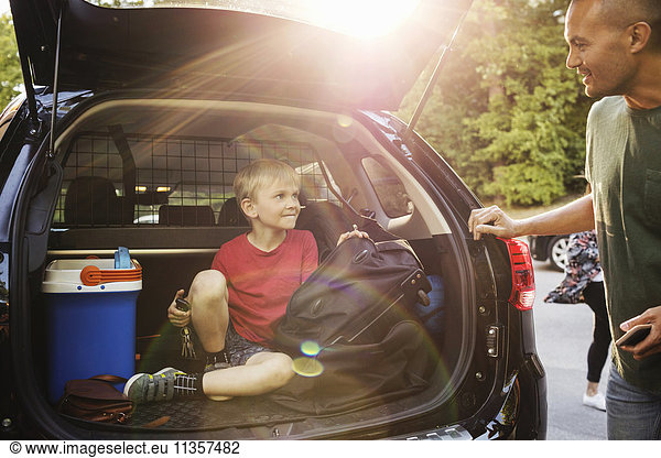 Happy father looking at boy sitting in car trunk