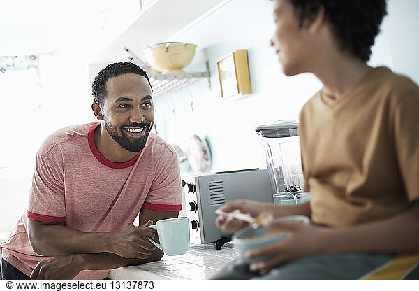 Happy father looking at son while having coffee at kitchen counter