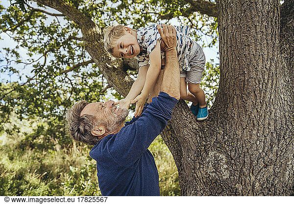 Happy father playing with son by tree