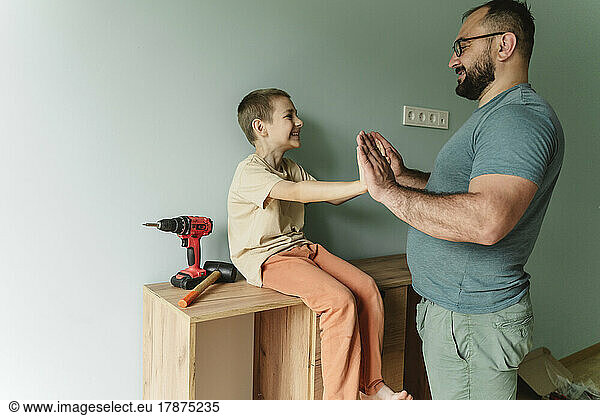 Happy father playing with son sitting on cabinet at home