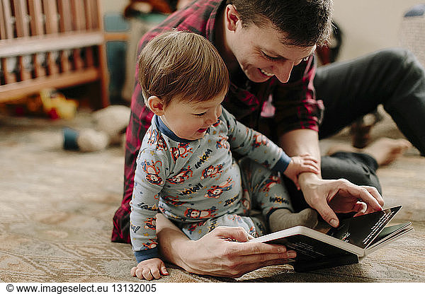 Happy father showing picture book to son while sitting on carpet at home
