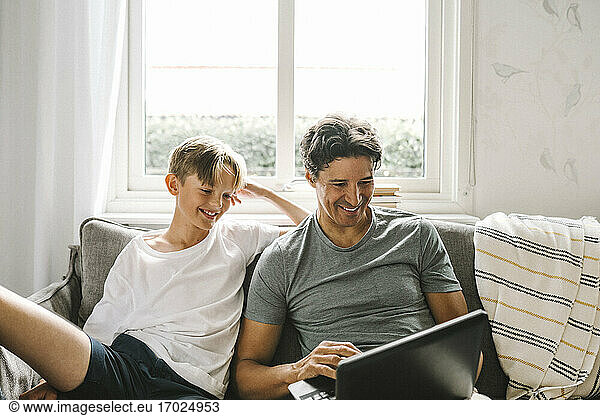 Happy father using laptop while sitting by son in living room