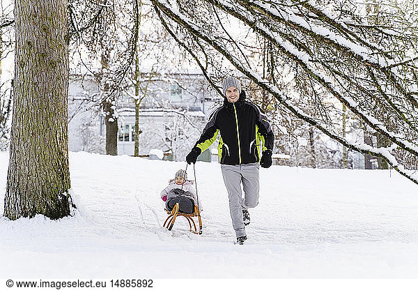 Happy father with daughter on sledge in winter landscape