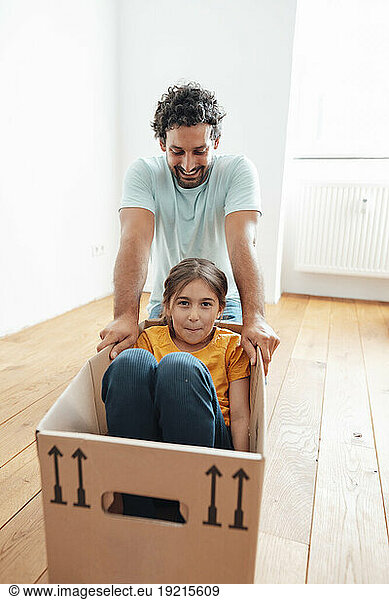 Happy father with daughter sitting in cardboard box at home