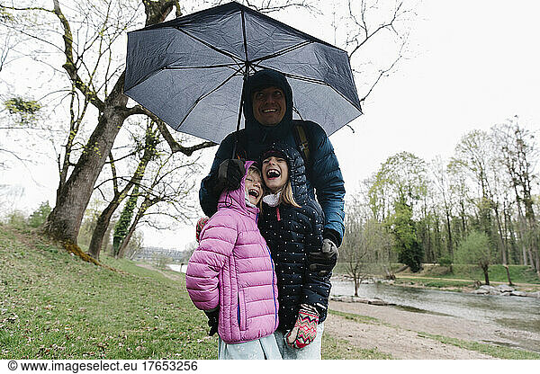 Happy father with daughters standing under umbrella