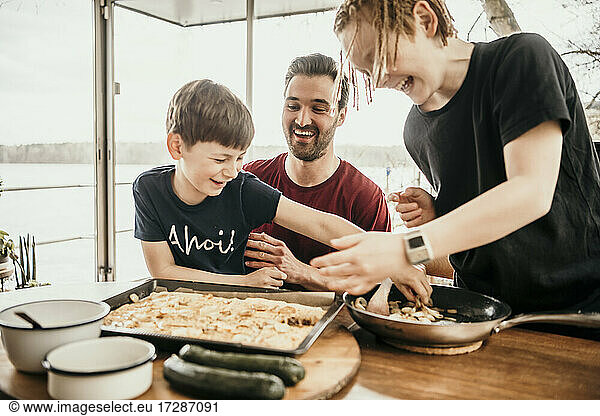 Happy father with playful sons preparing food at houseboat