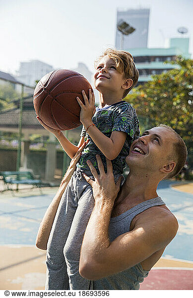 Happy father with son holding basketball on sunny day