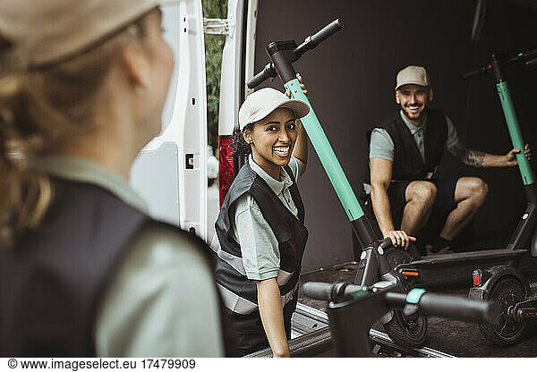 Happy female and male coworkers loading electric push scooter in delivery van