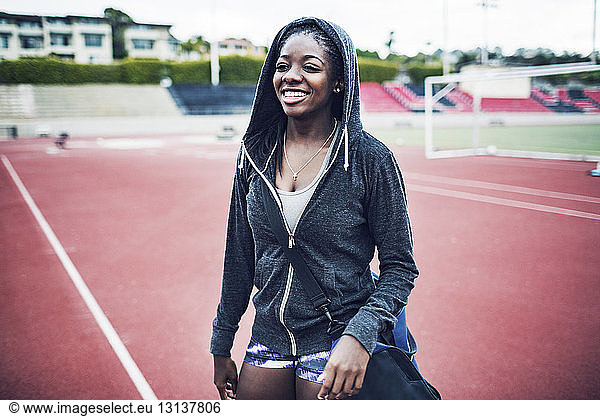 Happy female athlete in hooded jacket standing on running tracks