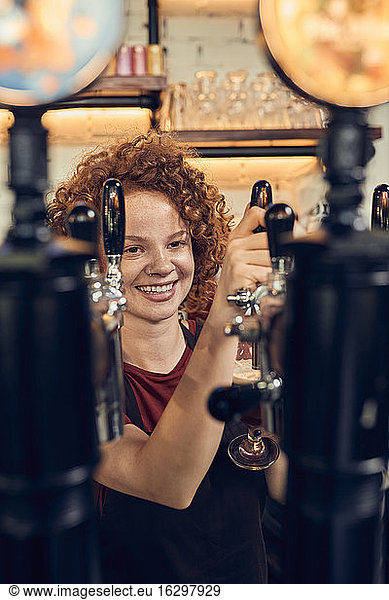 Happy female barkeeper tapping beer in a pub