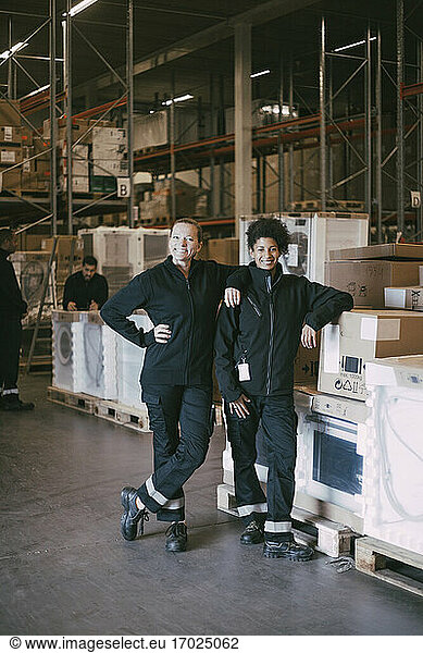 Happy female colleagues standing by box containers in warehouse