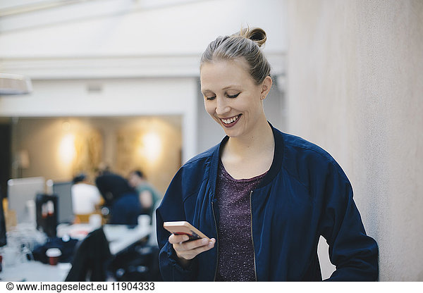 Happy female computer programmer using smart phone in creative office