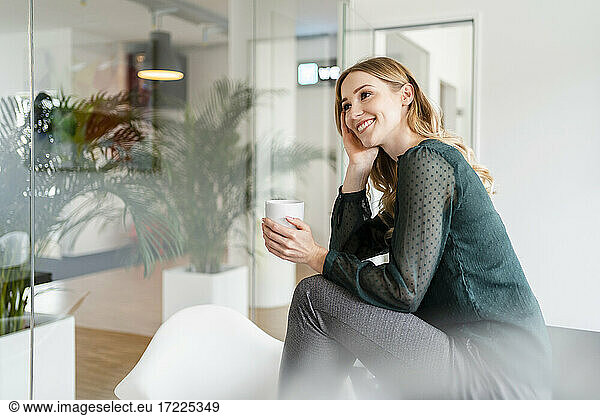 Happy female entrepreneur contemplating while having water in office