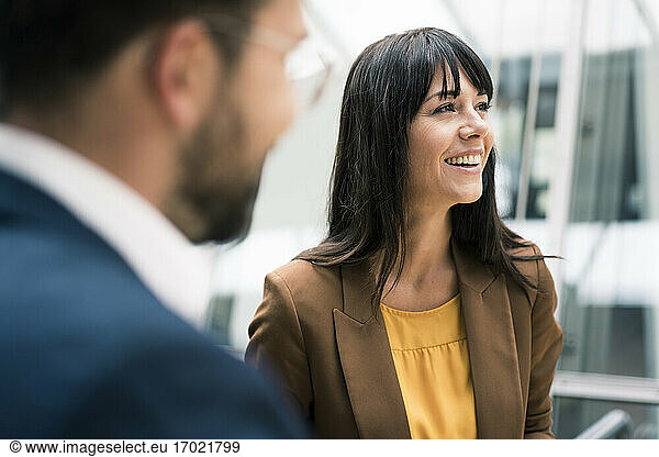 Happy female entrepreneur looking away while standing by male colleague in office