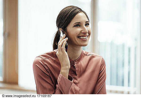 Happy female entrepreneur looking away while talking on mobile phone in office