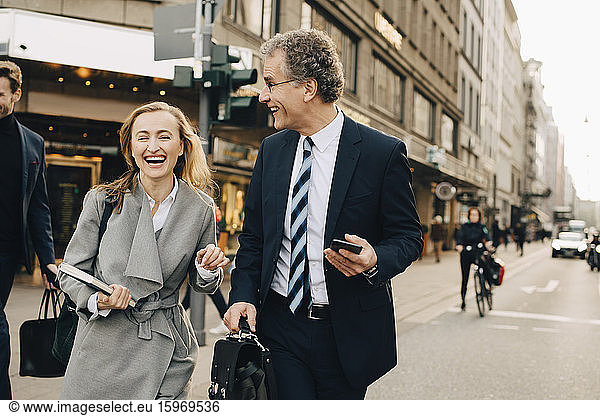 Happy female entrepreneur with male colleague crossing road in city