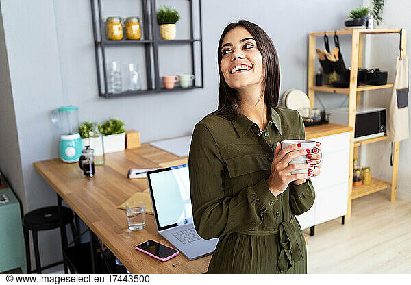 Happy female freelancer holding coffee mug at home