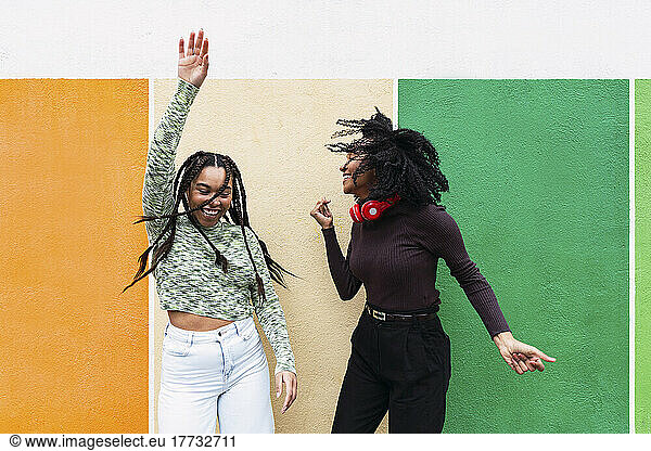 Happy female friends enjoying dance in front of multi colored wall