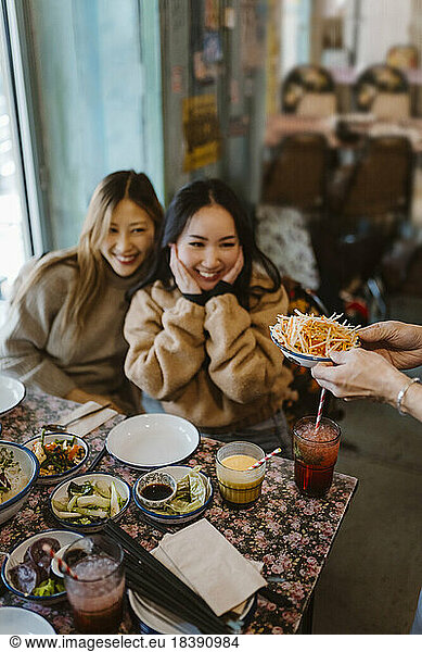 Happy female friends looking at food being served at restaurant