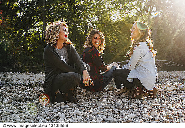Happy female friends sitting on pebbles during sunny day