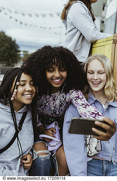 Happy female friends taking selfie on smart outdoors