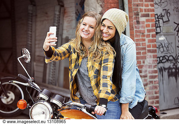 Happy female friends taking selfie while sitting on bike