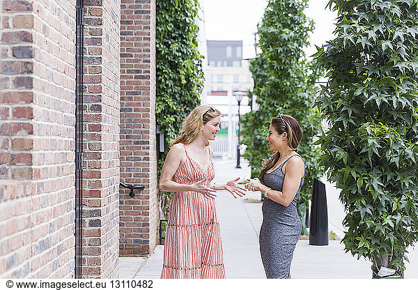 Happy female friends talking while standing at sidewalk