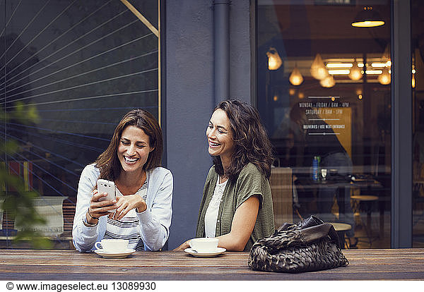Happy female friends using smart phone at sidewalk cafe