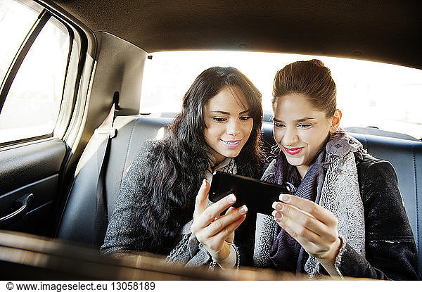 Happy female friends using smart phone while travelling in car