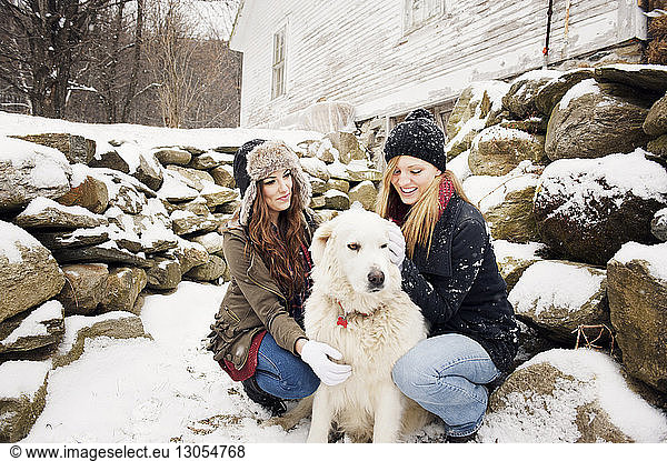 Happy female friends with dog by stones in winter