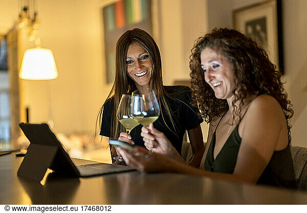Happy female friends with wineglasses using smart phone at table