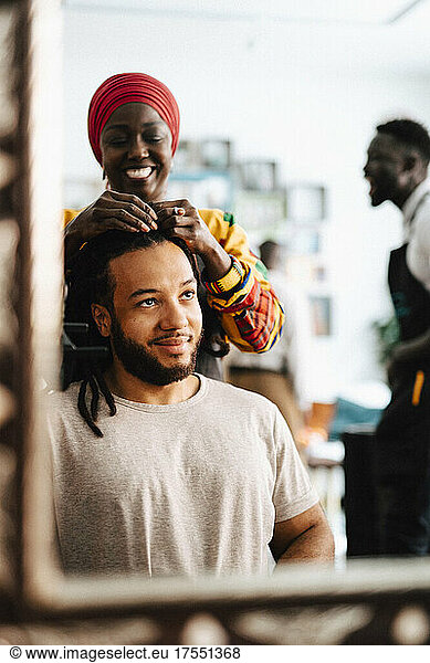Happy female hairdresser making locs of male customer at barber shop