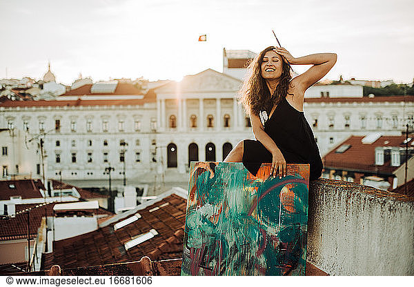 Happy female painter sitting on rooftop with city view of Lisbon