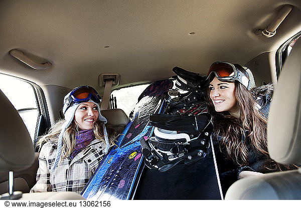 Happy female skiers sitting by snowboards in car