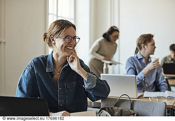 Happy female student with eyeglasses looking away while sitting in classroom