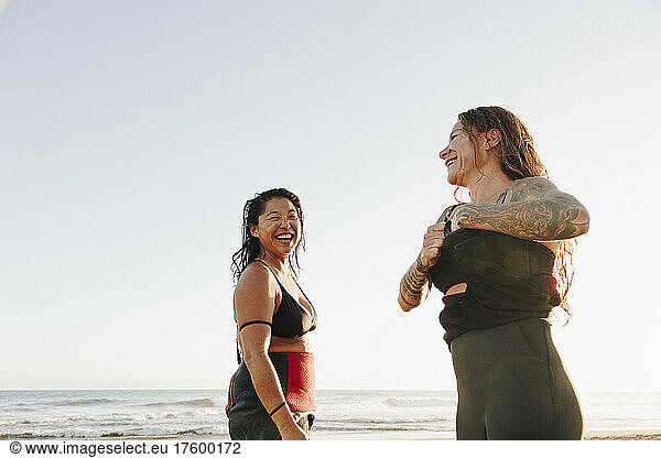Happy female surfers talking to each other undressing at beach