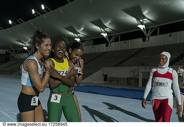 Happy female track and field athletes celebrating on track at night