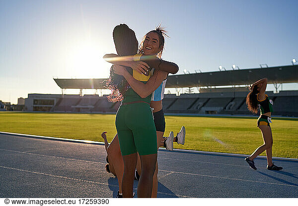Happy female track and field athletes hugging on sunny track
