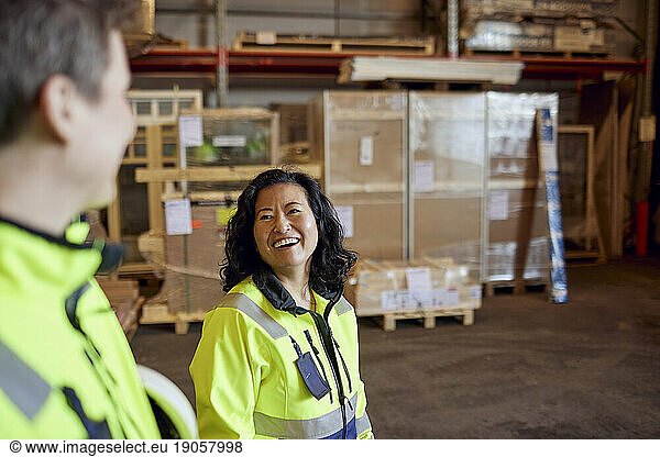 Happy female worker discussing with colleague while walking in distribution warehouse