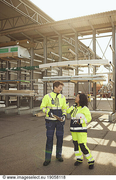Happy female workers in protective workwear discussing while standing at warehouse