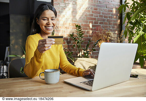 Happy freelancer doing online payment through credit card at loft office