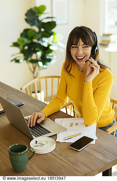 Happy freelancer listening through headset at home office