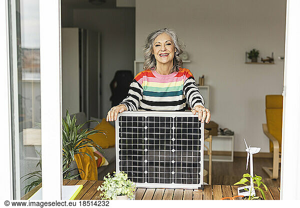Happy freelancer standing with solar panel at home