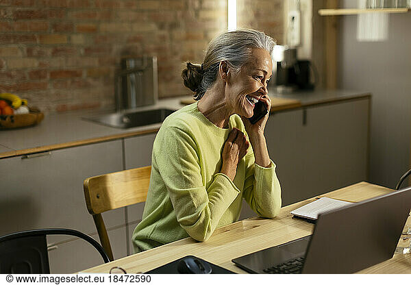 Happy freelancer talking on smart phone at desk in home
