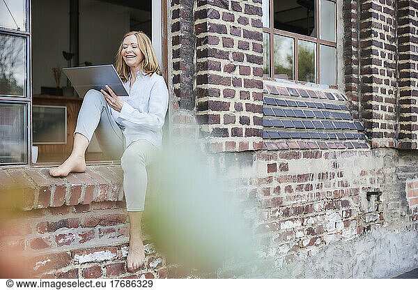 Happy freelancer using digital tablet sitting on doorway