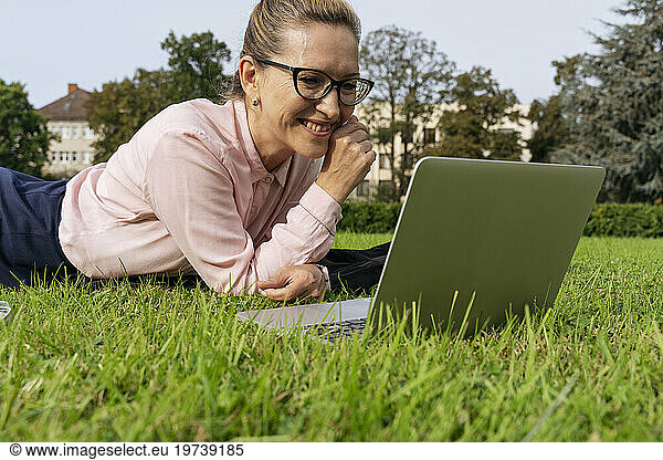 Happy freelancer using laptop lying on grass in park