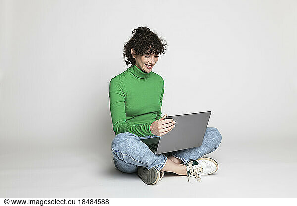 Happy freelancer using laptop sitting against white background