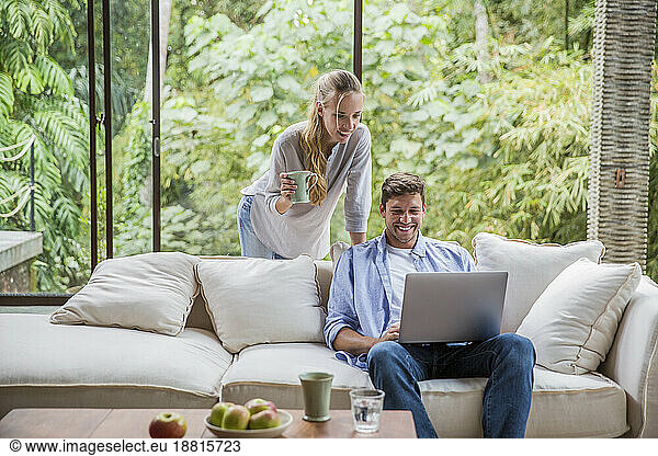 Happy freelancer using laptop with woman holding coffee cup at home