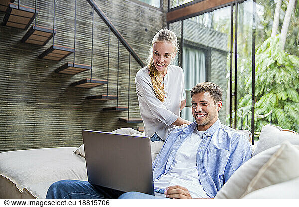 Happy freelancer using laptop with woman on sofa at home